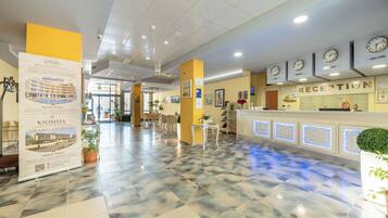 Zona de recepción de un hotel con mostrador de entrada, relojes y suelo de baldosas.
