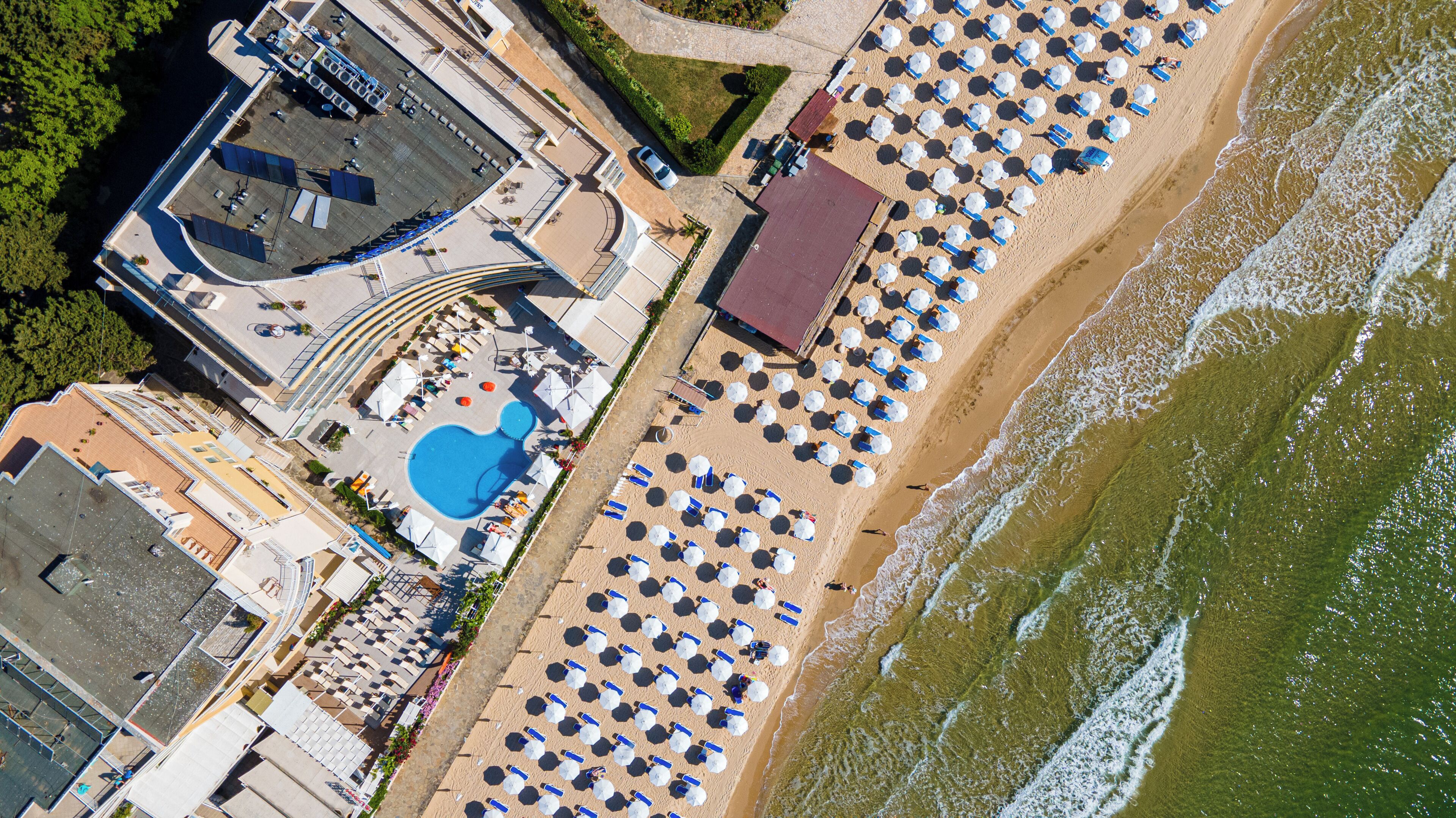 An aerial view of a beachside hotel with a swimming pool, sun loungers, and umbrellas.