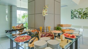Un buffet proposant une variété de plats, notamment des viandes, des fromages et des fruits, disposés sur une table en verre dans une cuisine moderne.
