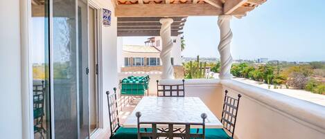 A balcony with a table and chairs, a pergola overhead, and a view of the cityscape.