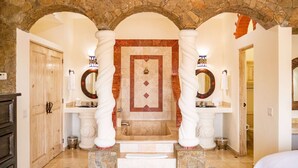 Un baño espacioso con un arco de piedra, un espejo grande y una bañera.