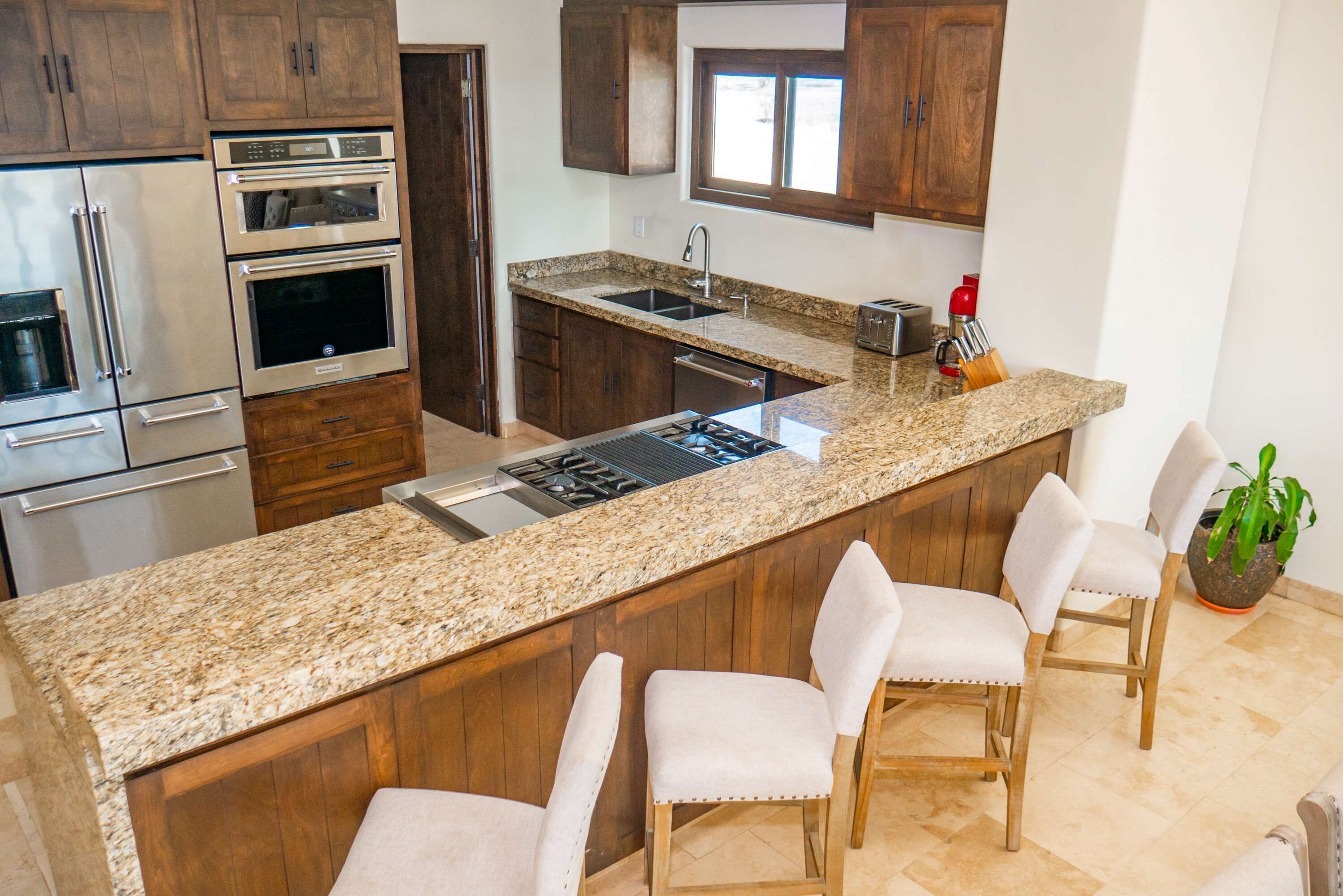 A kitchen with granite countertops, stainless steel appliances, wooden cabinets, and a bar area with bar stools.