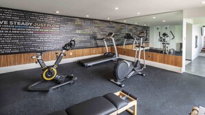 Une salle de sport équipée d’appareils de cardio, d’un banc et dont les murs sont ornés de citations motivantes.