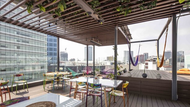 Une terrasse sur le toit, agrémentée de tables et de chaises, une pergola ornée de plantes suspendues et une vue imprenable sur le panorama urbain.