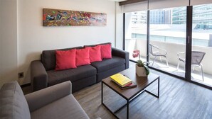 Un salon moderne avec un canapé gris, des coussins rouges, une table basse sur laquelle repose un livre, et une grande fenêtre offrant une vue sur la ville.