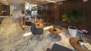 Un vestíbulo moderno con suelo de mármol, una recepción, zona de estar con sillas y mesas, y una planta grande en maceta.