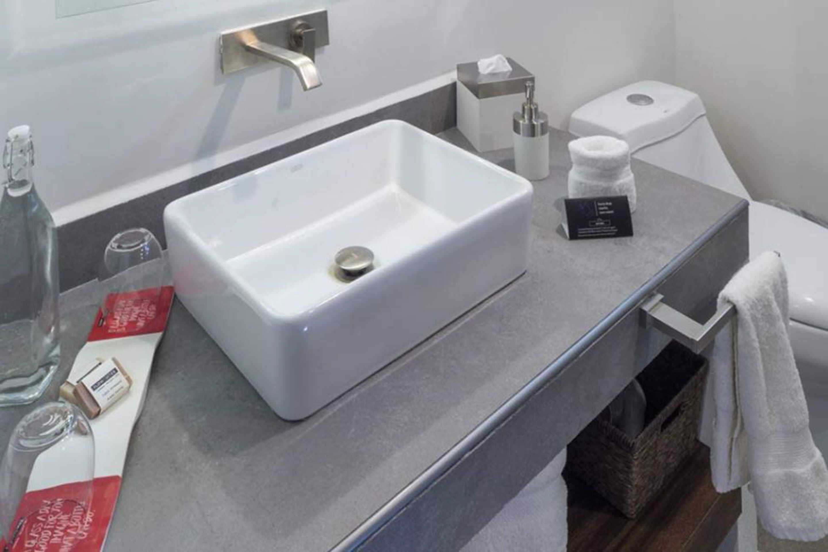 Ein modernes Badezimmer mit einem rechteckigen weißen Waschbecken, einem Handtuchhalter, einer Taschentuchbox und einer Seifenspender.