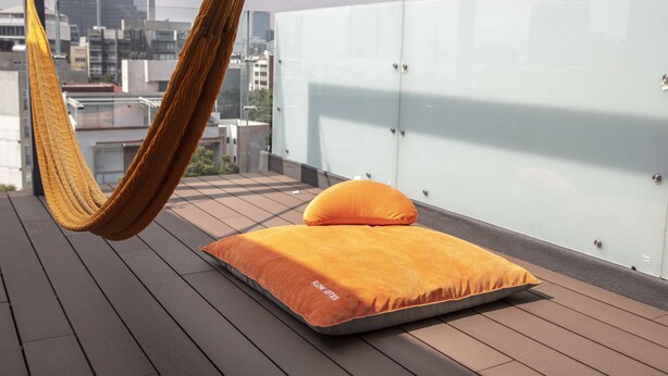 Una hamaca en un balcón con colchón y almohadas, con vistas a un paisaje urbano.