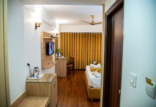 A hotel room with a wooden desk, a television, a bed with towels, a chair, and a curtain. - Sun Park Resort, Chandigarh (Dera Bassi)