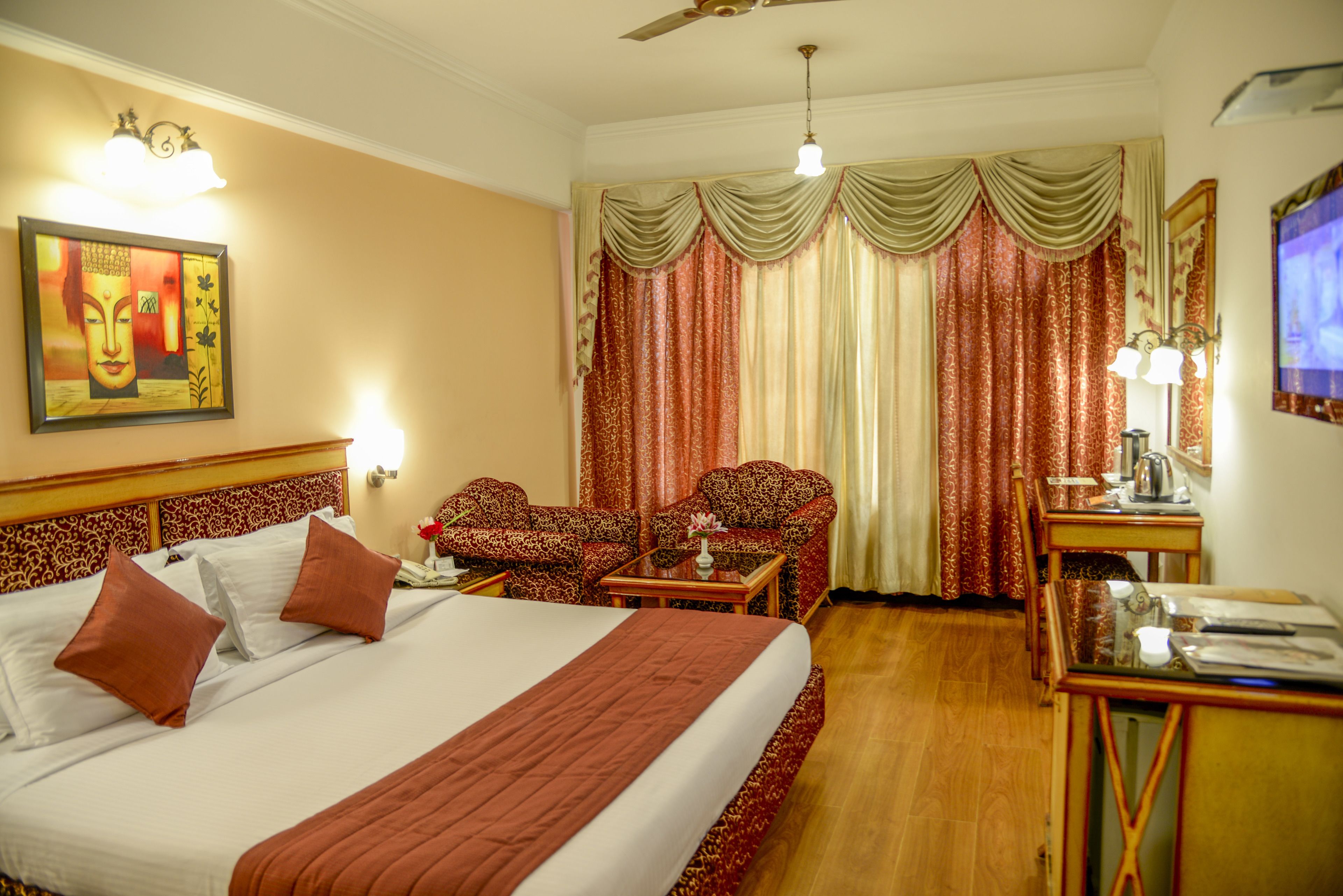A hotel room with a large bed, two armchairs, a desk, and a television.