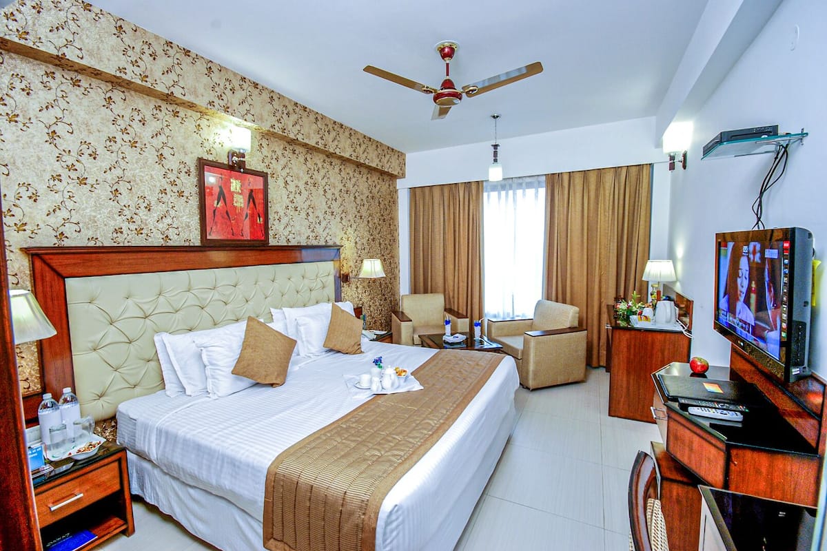 A hotel room with a large bed, a TV, a desk, and a chair.