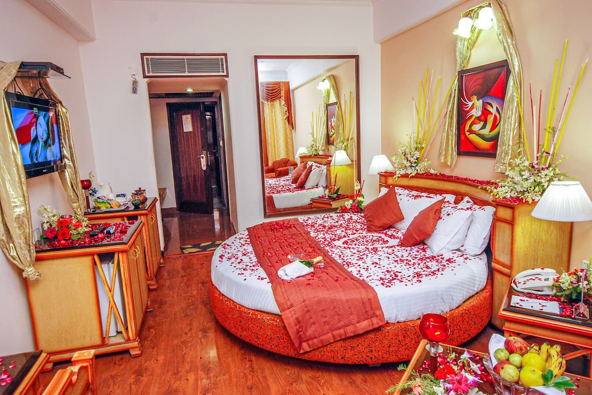 A hotel room with a round bed, a TV, a mirror, and a wooden floor.