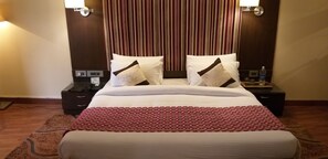 Quarto de hotel com uma cama grande, duas mesas de cabeceira, uma colcha de cama estampada em vermelho e um cortinado listrado ao fundo.