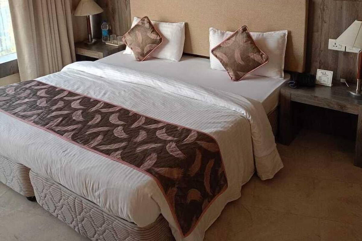 A hotel room with a large bed, a wooden headboard, two framed pictures, a nightstand, and a lamp.