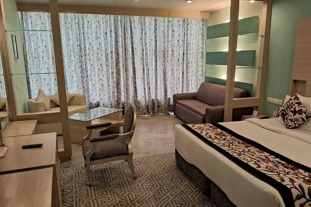 A hotel room with a bed, a sofa, a dining table, and a chair.