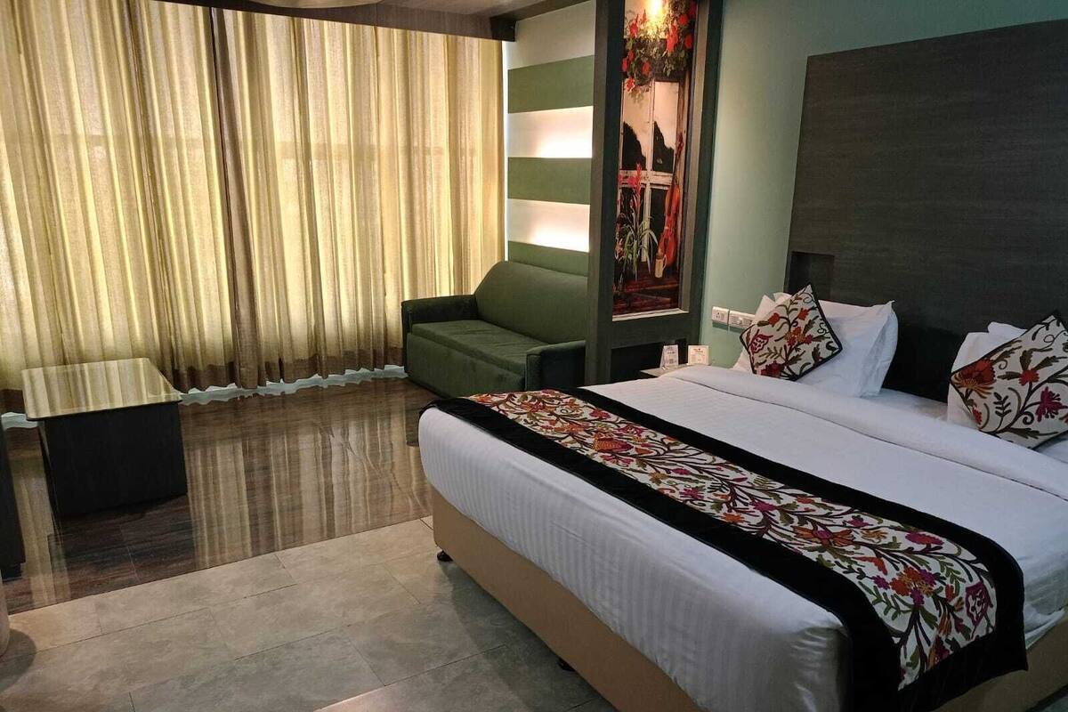 A hotel room with a large bed, a green sofa, a small table, and a window with curtains.