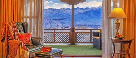 A room with a view of mountains, a leather sofa, a patterned rug, and a table with fruit.