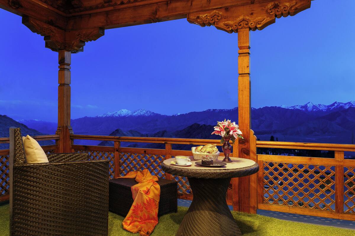 A wooden gazebo with a wicker chair and a table with a vase and a basket of bread.