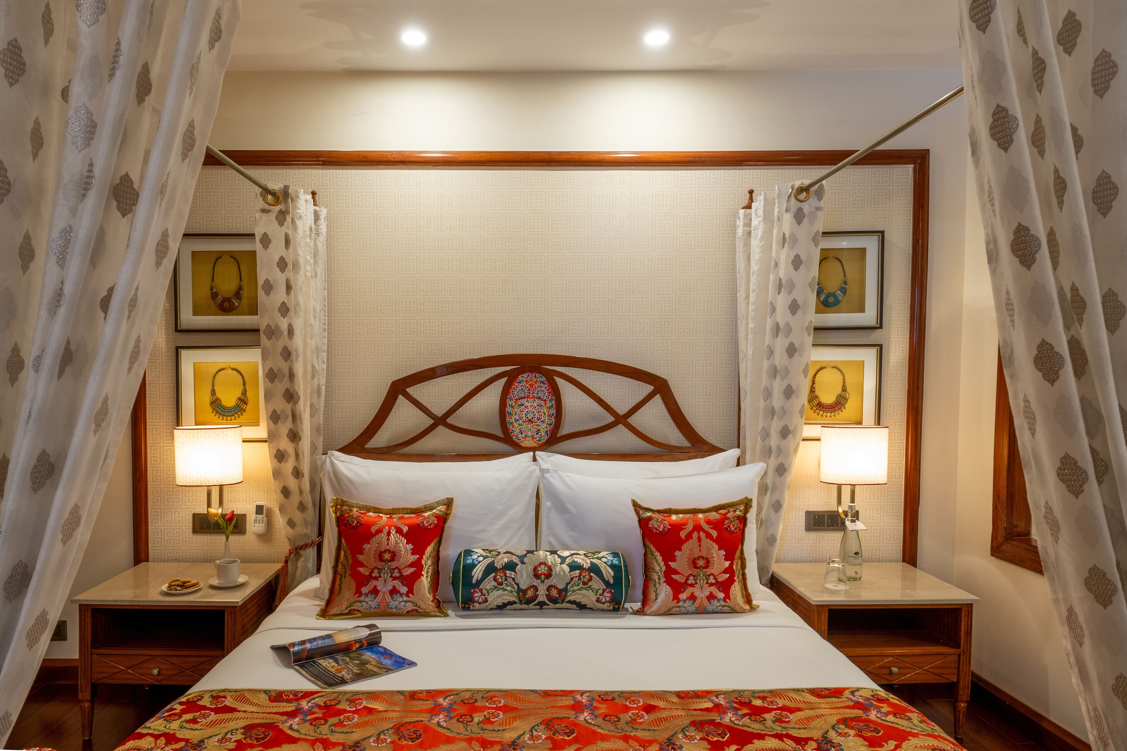 A hotel room with a bed, two bedside tables, a nightstand, and a headboard with a decorative design.