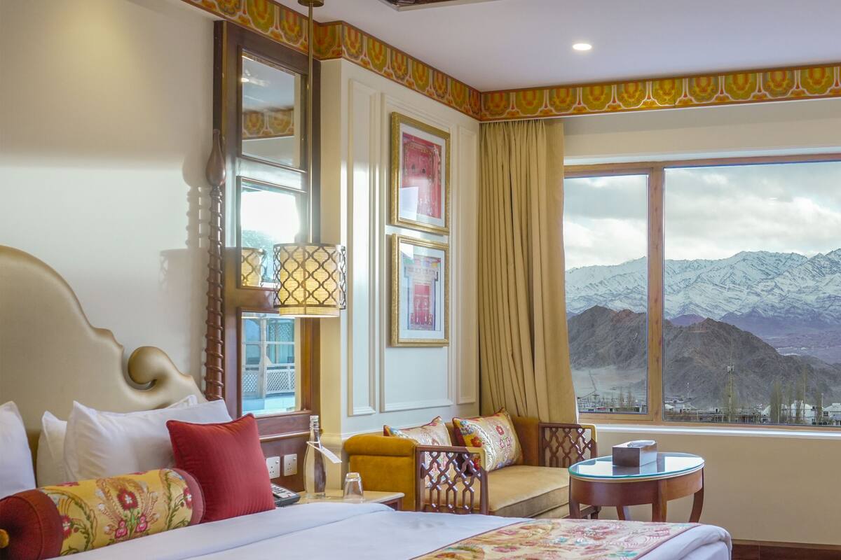 A hotel room with a large bed, a sofa, a small table, and a view of mountains through the window.