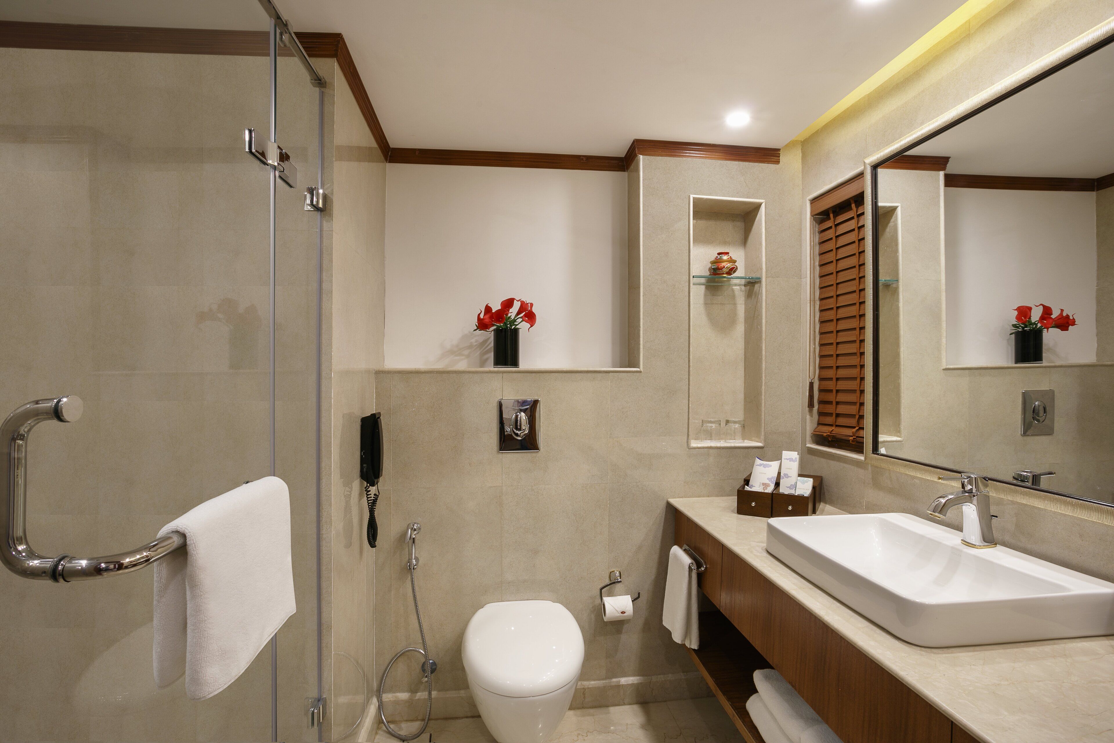 Un baño moderno con mampara de vidrio, inodoro blanco, lavamanos grande con espejo y toallero.