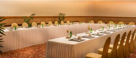 A long conference table set with chairs, white tablecloths, and small centerpieces.