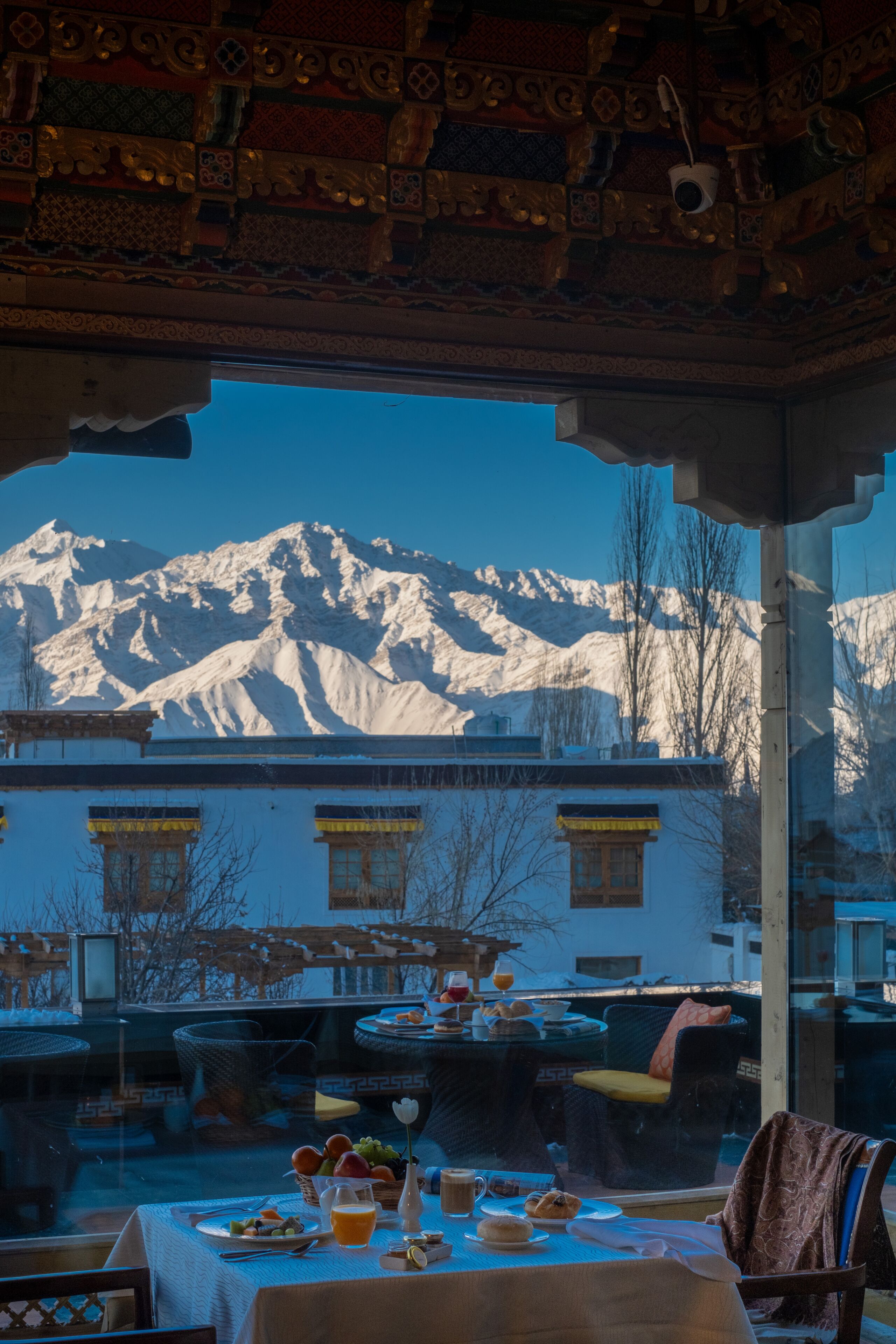A dining area with a table set for breakfast, a mountain view, and traditional architecture.