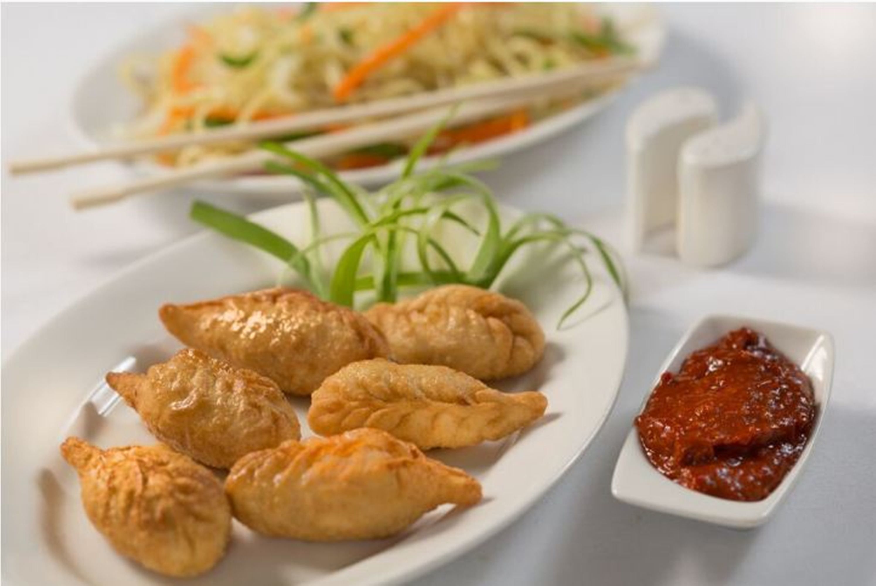 A plate of golden-brown pastries with a side of red sauce, accompanied by a plate of coleslaw and chopsticks.