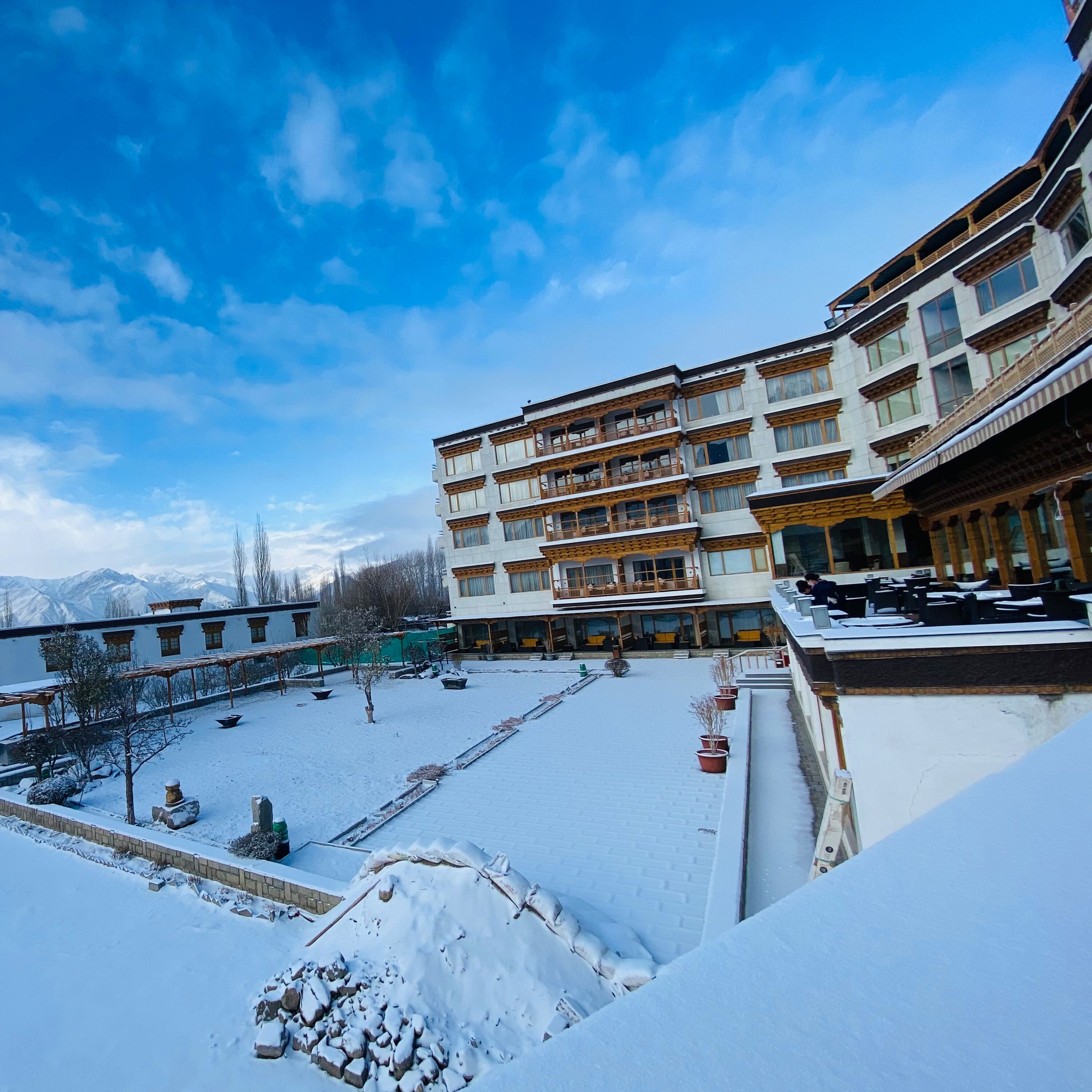 A multi-story building with balconies, a courtyard with snow, and mountains in the background.