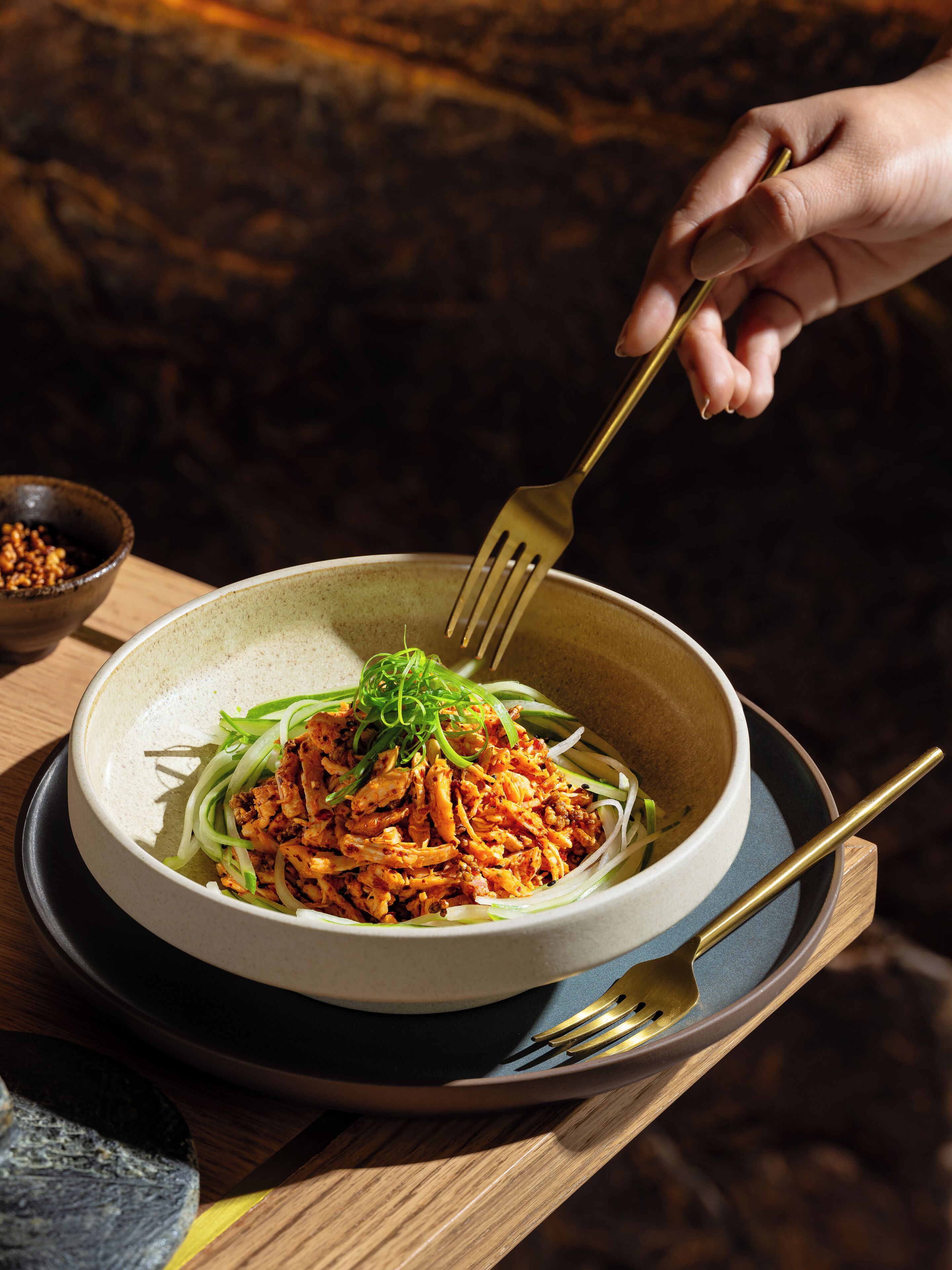 A bowl of food with a fork and spoon on a wooden table.