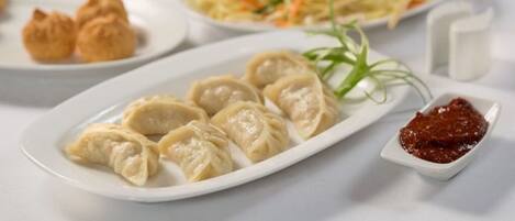 A table with various dishes including dumplings, a noodle dish, and a small bowl of sauce.