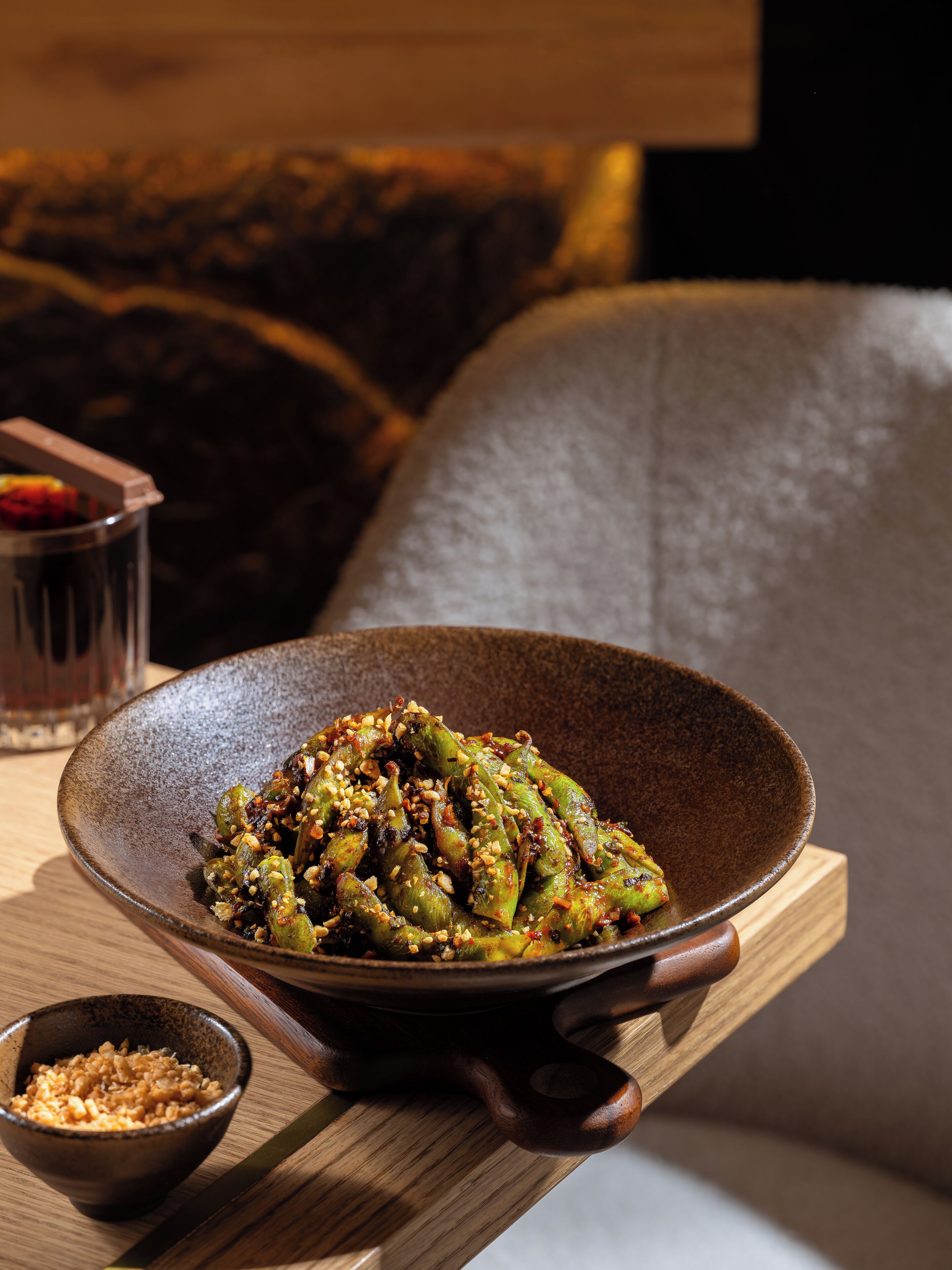 A bowl of food on a wooden tray with a glass and a small bowl of grains.