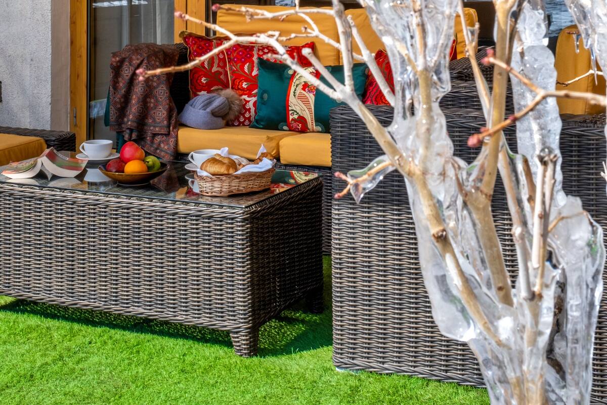 A cozy outdoor seating area with wicker furniture, a glass table, and a view of snow-capped mountains through large windows.
