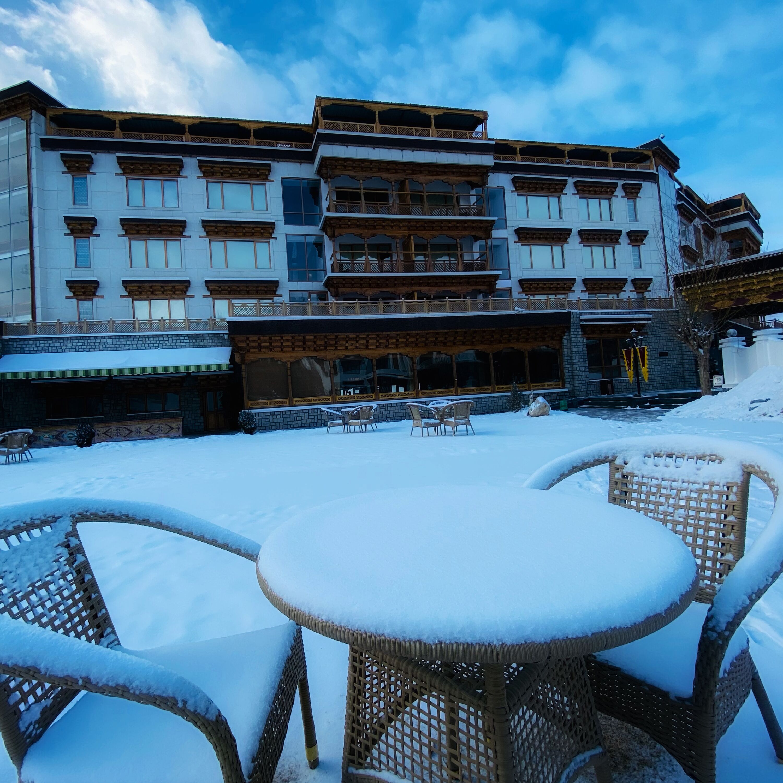 A hotel with a traditional architectural style, featuring multiple balconies and a covered outdoor seating area with wicker furniture.