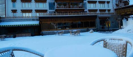 A hotel with a traditional architectural style, featuring multiple balconies and a covered outdoor seating area with wicker furniture.
