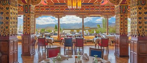 A restaurant with ornate decor, tables set for dining, and a mountain view.