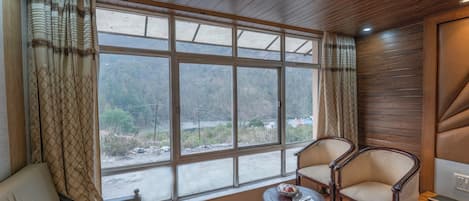 Una habitación con un ventanal grande, dos sillas, una mesita y una cama.