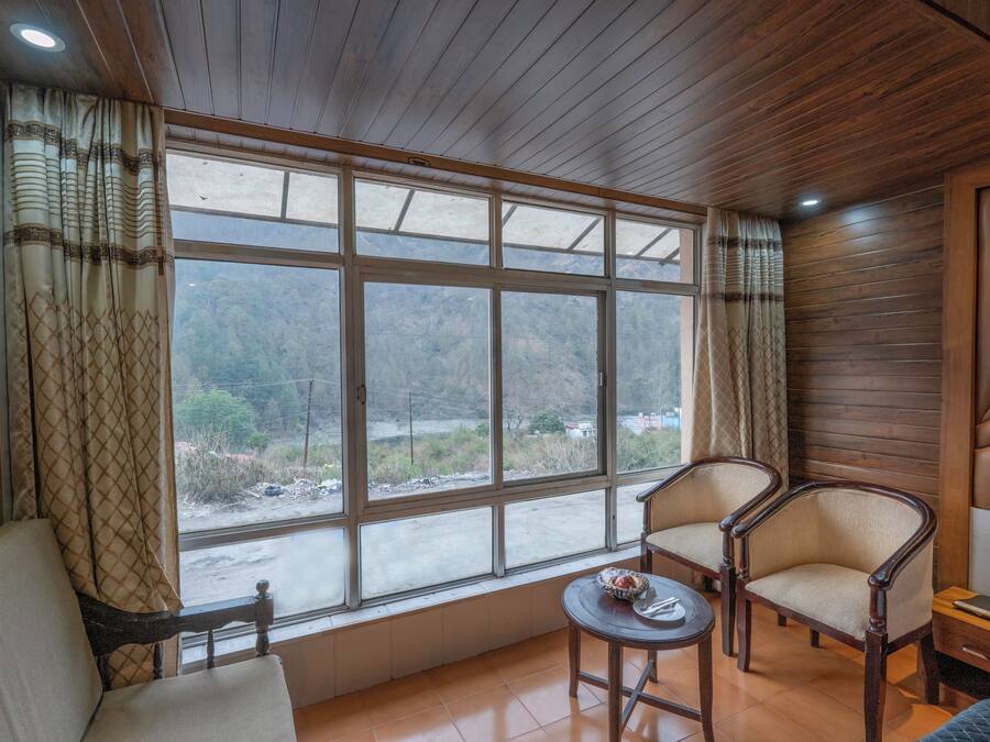Una habitación con un ventanal grande, dos sillas, una mesita y una cama.