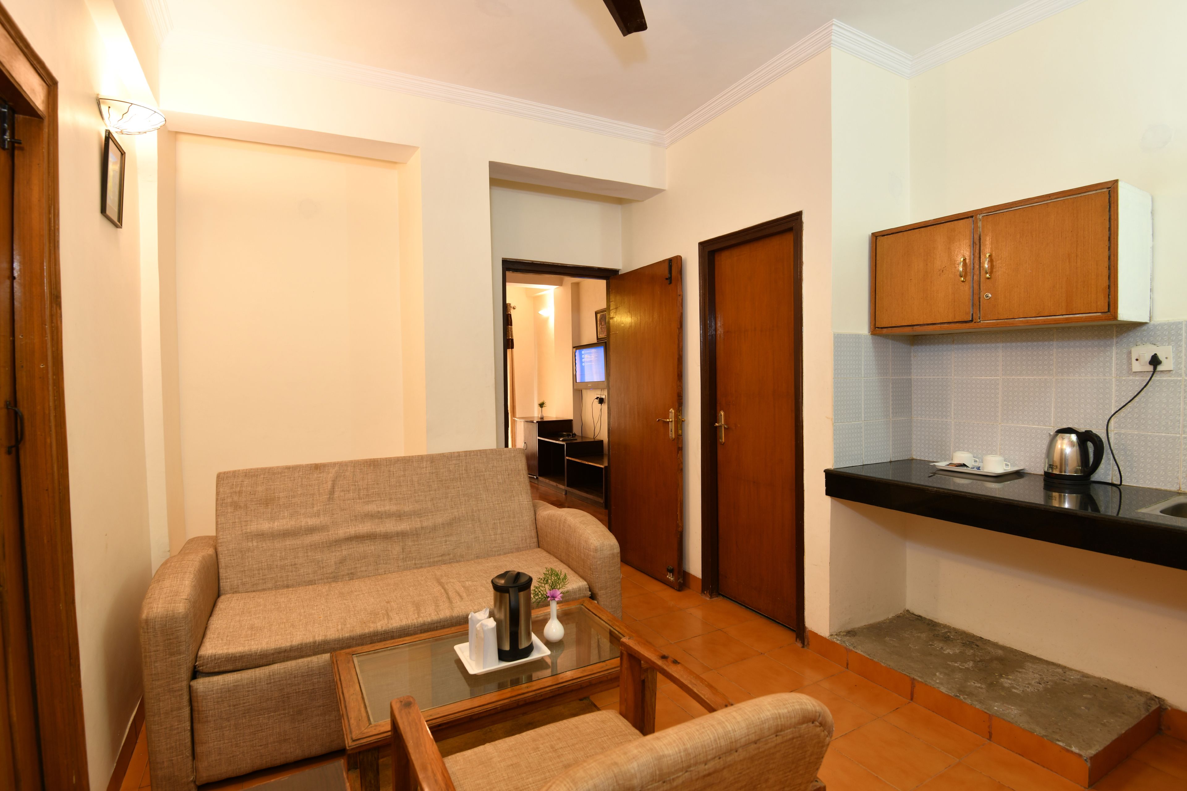 A compact living space with a sofa, a small table, a kitchenette, and a door leading to another room.