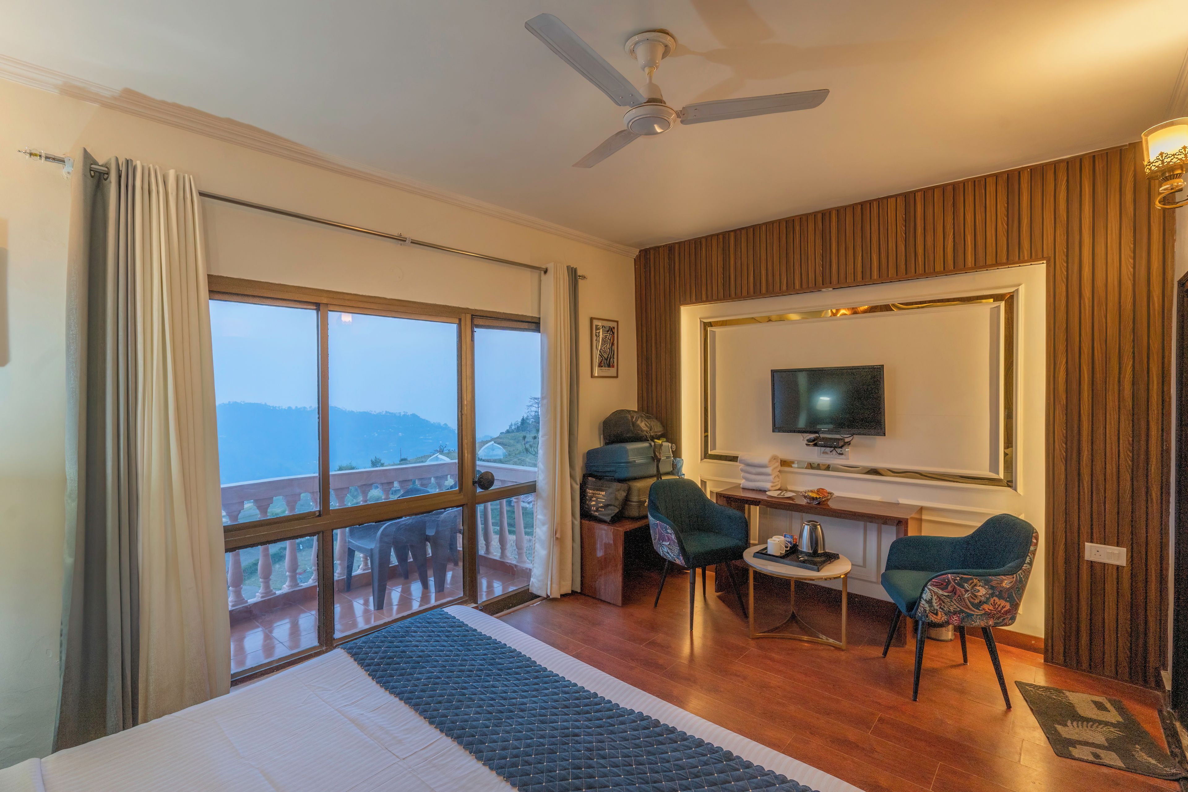 A hotel room with a balcony, a ceiling fan, a TV, and a desk with a chair.