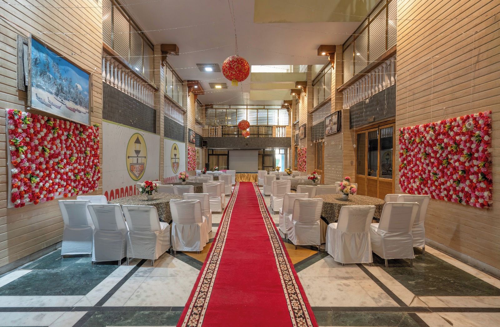 A banquet hall with white chairs, a red carpet, and floral decorations.