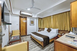 Een hotelkamer met een bed, een bureau, een stoel, een televisie en een airconditioning.