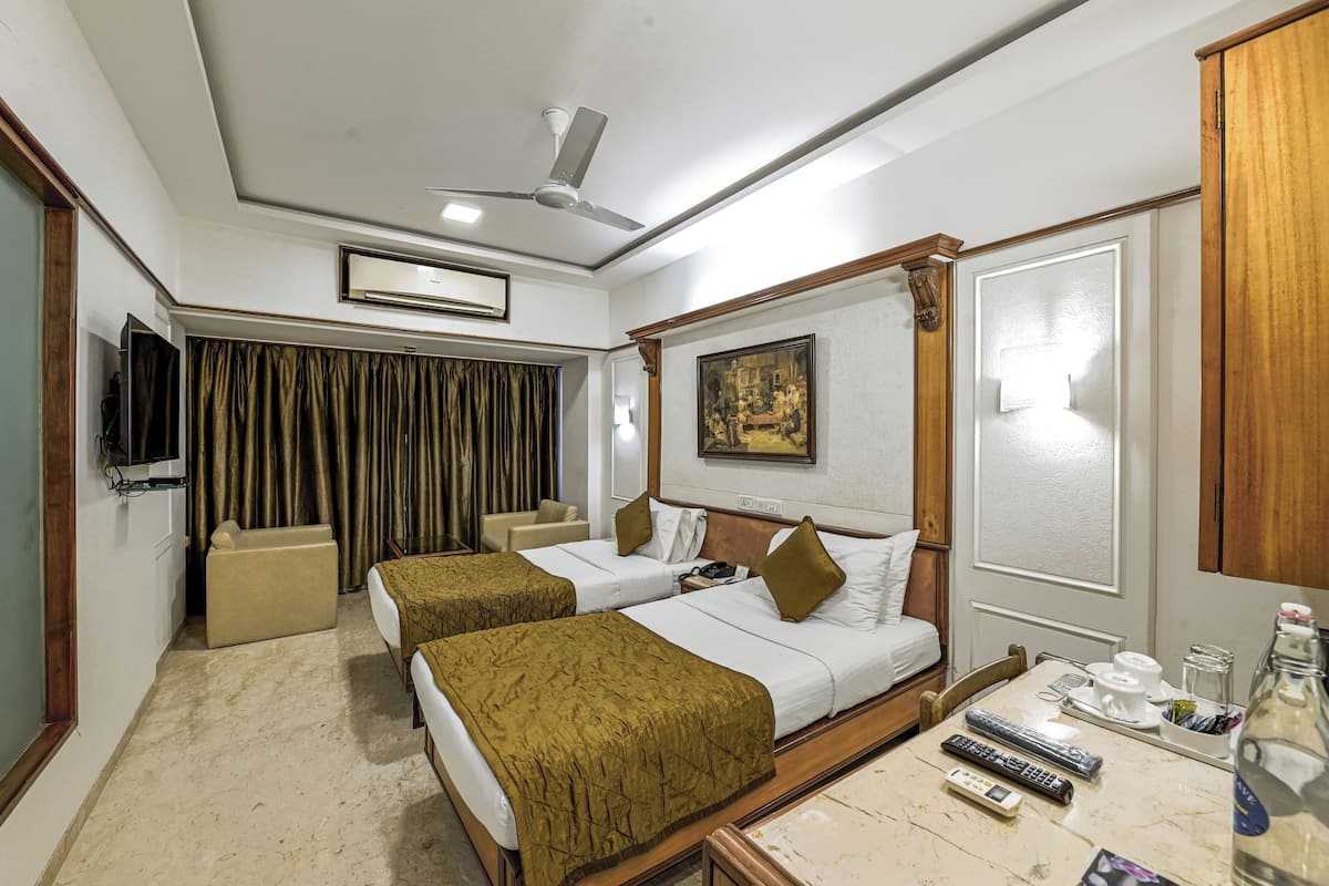 A hotel room with two beds, a TV, a ceiling fan, and a painting on the wall.