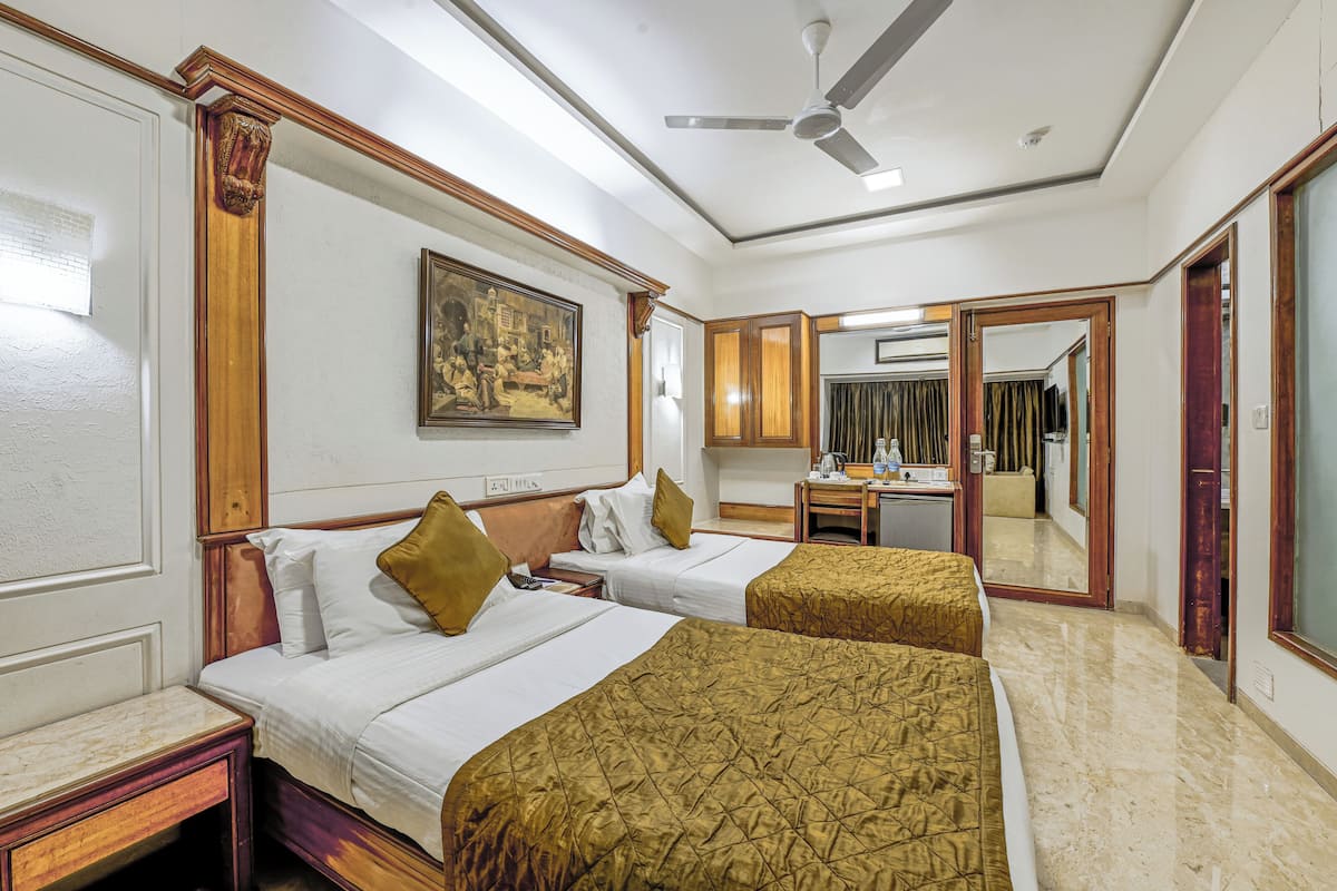 A hotel room with two beds, a desk, a mirror, and a ceiling fan.