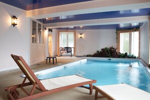 An indoor swimming pool with lounge chairs, a chair, and a small table. - Aviation Hotel (La Bourboule)