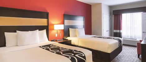 Quarto de hotel com duas camas, uma parede de destaque vermelha, um tapete estampado e uma janela com cortinas.