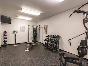 A gym with exercise equipment, a wall-mounted TV, and a poster. - La Quinta Inn & Suites by Wyndham Fargo-Medical Center (Fargo)