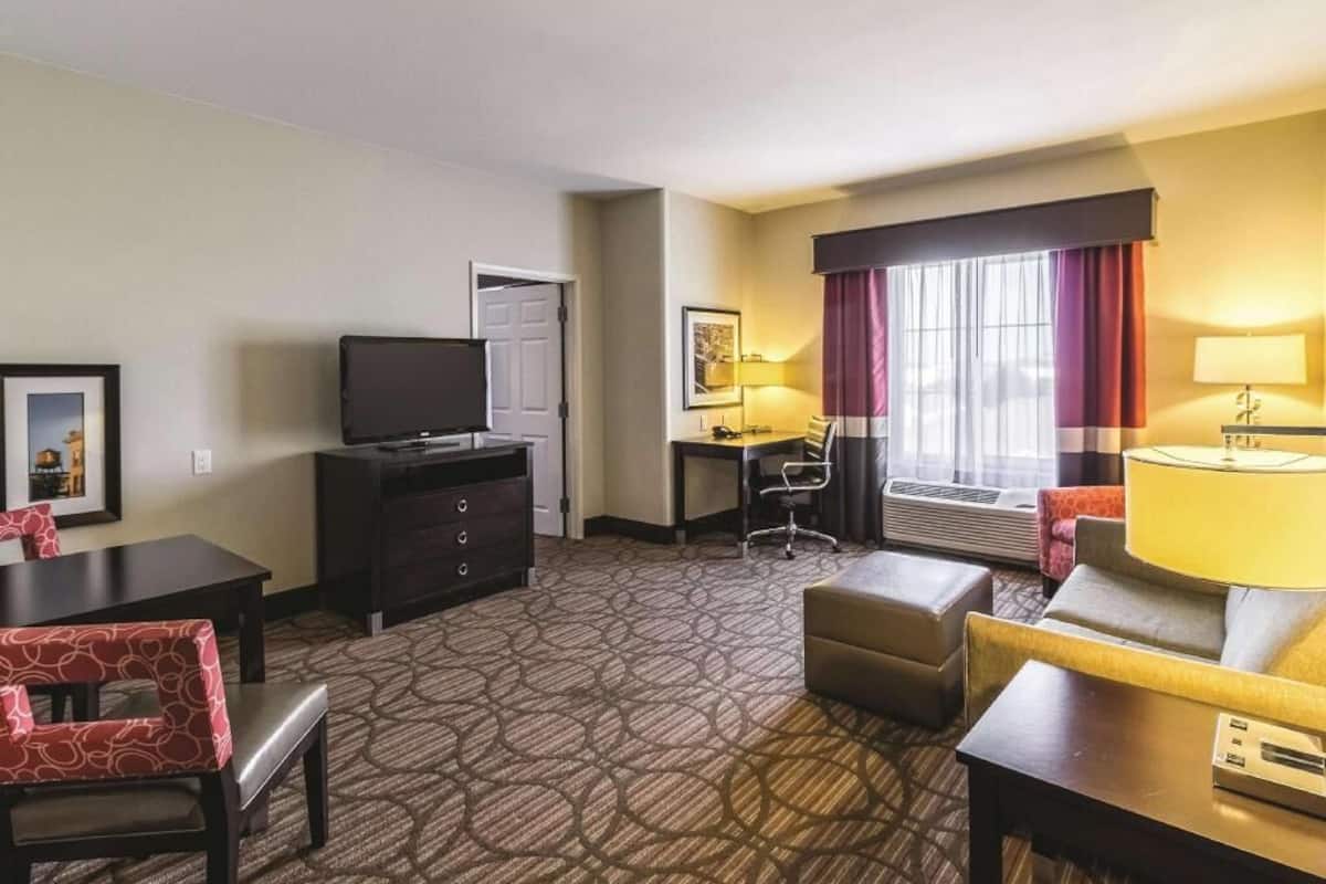 A hotel room with a television, a desk, a chair, a sofa, and a window with curtains.