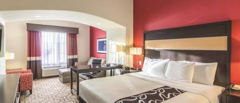 A hotel room with a large bed, a desk, a chair, a desk lamp, and a telephone.