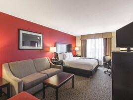 A hotel room with a bed, a sofa, a desk, a TV, and a window with curtains.
